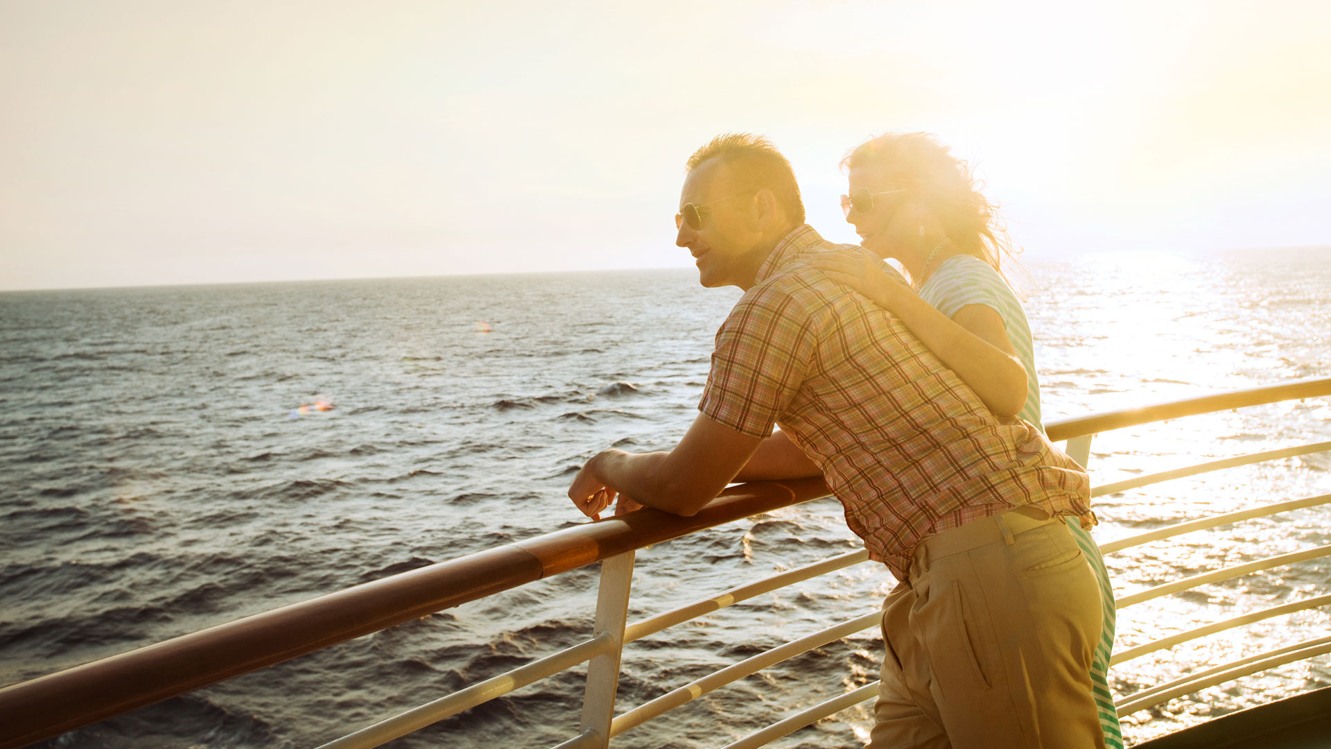 Couple looking out to the sea from a deck on a cruise ship at sunset