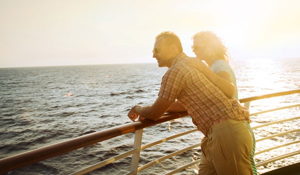 Couple looking out to the sea from a deck on a cruise ship at sunset
