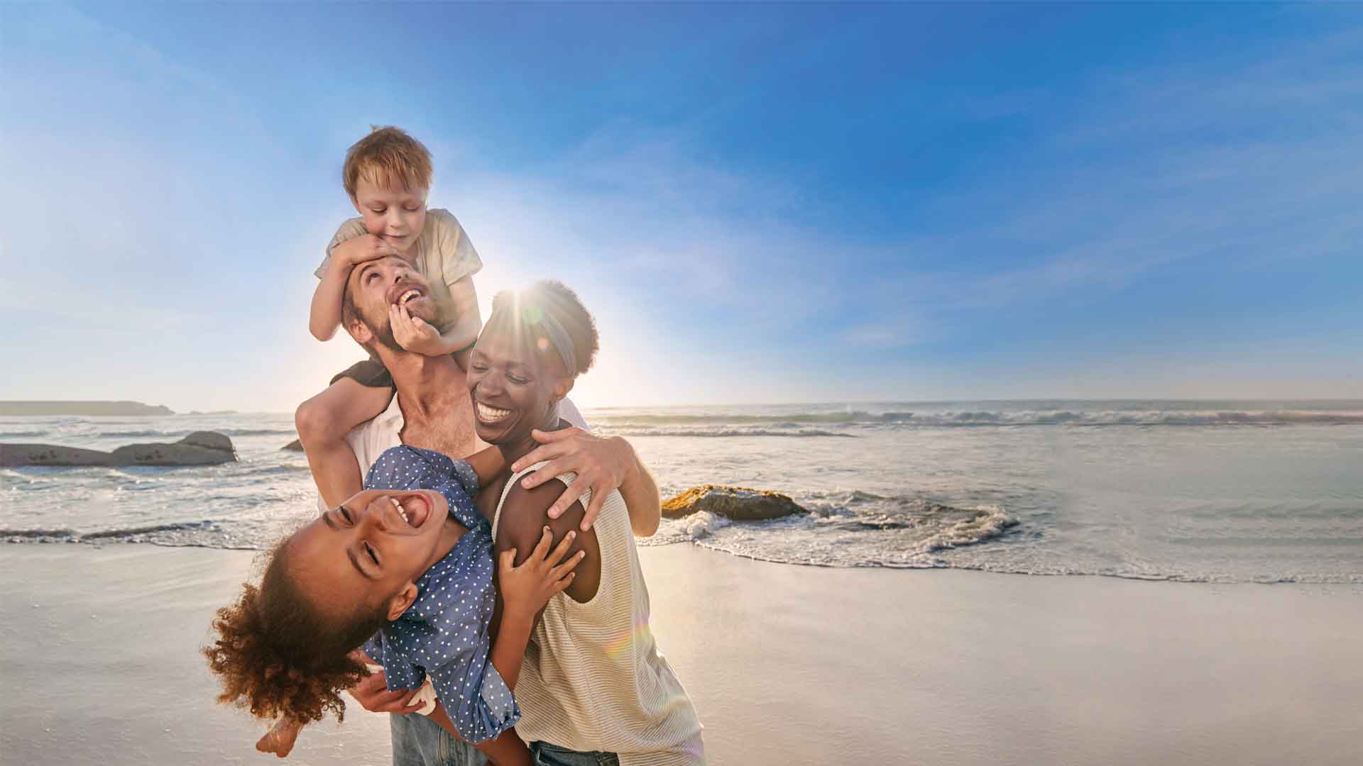 A family of 4 of mixed ethnicity laughing happily on the beach. 