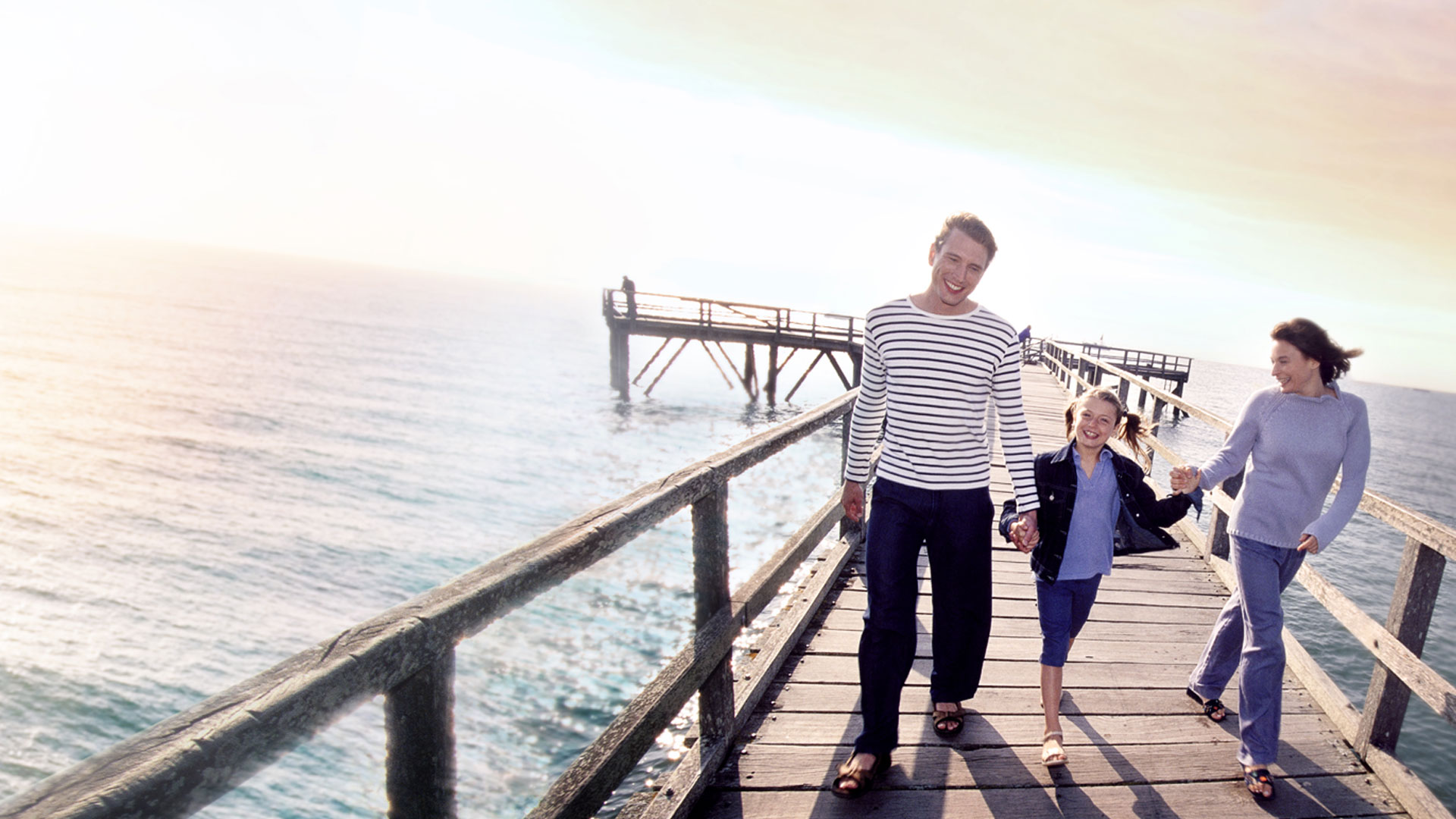 A family of 3 with a young boy walking down a boardwalk in an evening