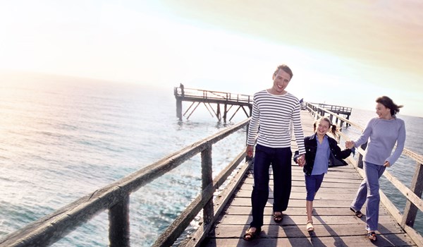 A family of 3 with a young boy walking down a boardwalk in an evening
