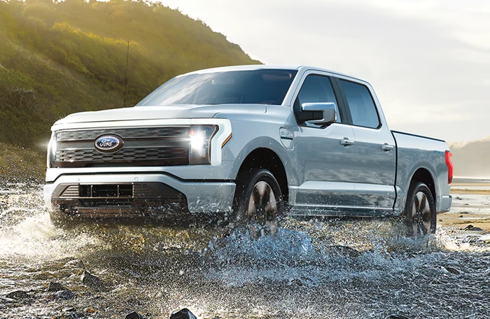 A Ford F-150 riding through a shallow creek on a countryside landscape.