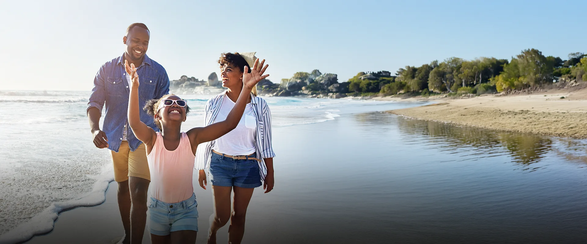 A smiling family walks on a sunny beach.