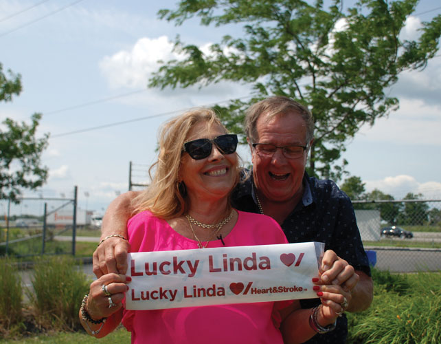 Husband and wife smiling and holding small sign saying ‘Lucky Linda’. 