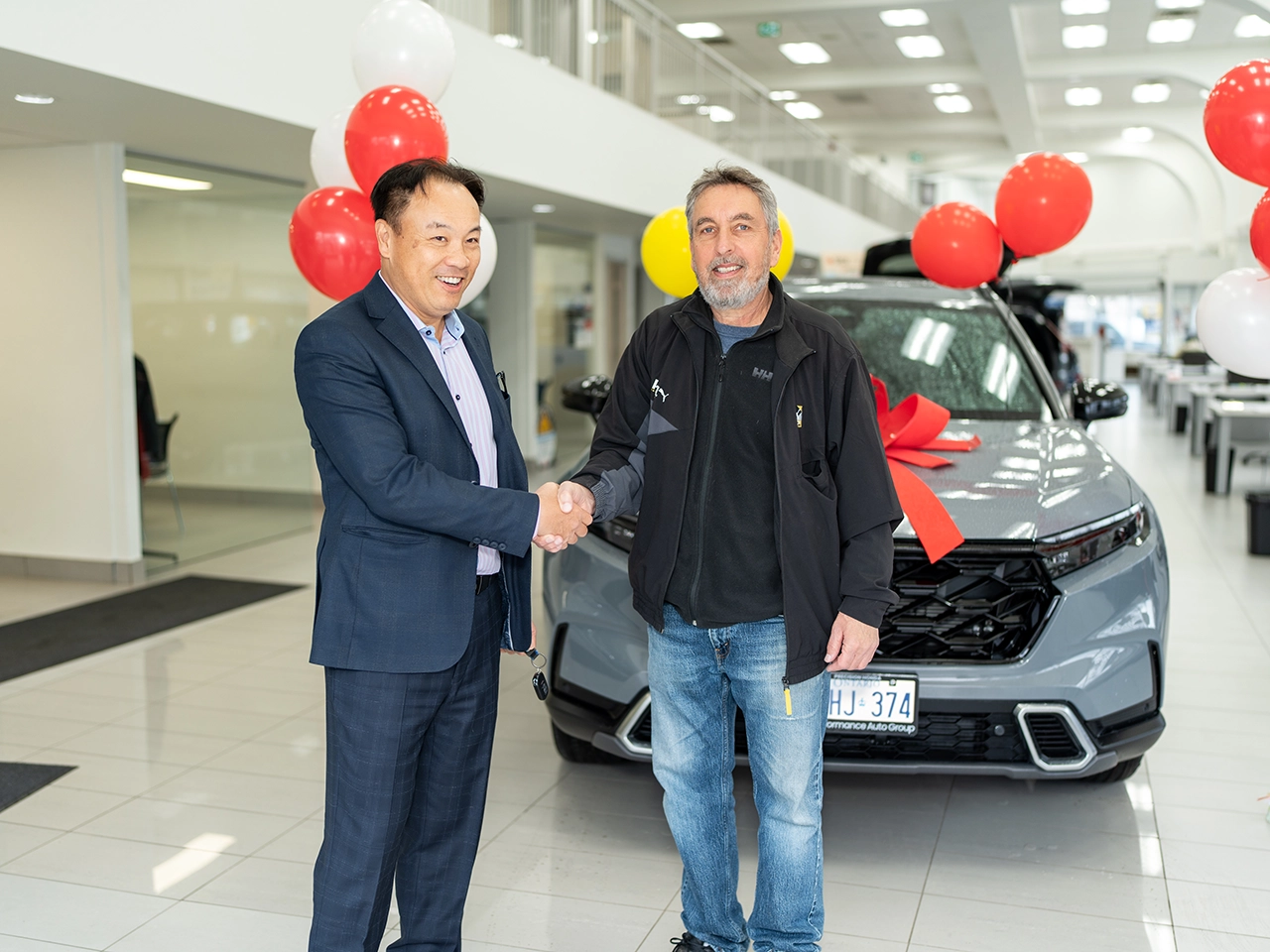 Lottery winner shakes hands with a dealership representative while standing in front of a newly awarded vehicle. 